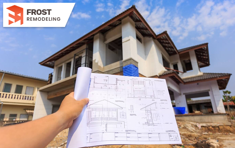 Hand holding architectural plans in front of an under-construction building